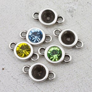 May include: Silver-toned jewelry connectors with a circular design. Some connectors feature colorful gemstones in blue, yellow, and green. The connectors have small loops on each side for attaching to other jewelry components.