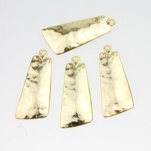 Puede incluir: Cuatro colgantes de metal de color dorado con textura martillada. Los colgantes son rectangulares con esquinas redondeadas y tienen un agujero en la parte superior para sujetarlos a una cadena o cordón.