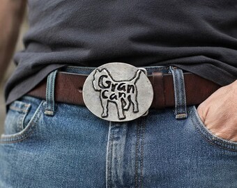 May include: A dark brown leather belt featuring a large, oval-shaped silver-toned metal buckle. The buckle displays a raised silhouette of a dog with the text "Gran Can" embossed in black lettering across the centre of the dog's body.