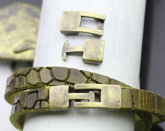 Könnte beinhalten: Nahaufnahme eines grün-braunen Lederarmbands mit einem einzigartigen strukturierten Muster. Das Armband hat einen rechteckigen antiken Messingverschluss. Zwei zusätzliche Verschlüsse werden über dem Armband angezeigt.
