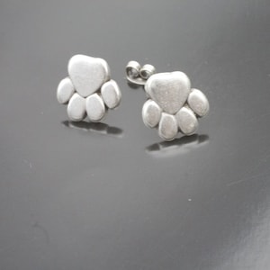 Op de afbeelding: Een paar zilveren oorbellen met een pootprint. De oorbellen zijn klein en delicaat en zouden een geweldig cadeau zijn voor elke hondenliefhebber.