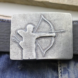 May include: A silver metal belt buckle with a raised design of an archer aiming an arrow. The buckle is rectangular and has a smooth, polished surface.