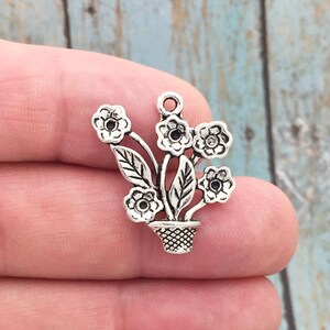 May include: Silver charm featuring a bouquet of flowers in a pot. The flowers are detailed with intricate designs and have a vintage aesthetic.