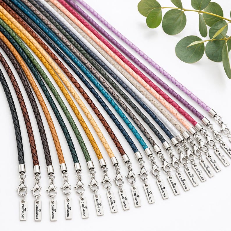 Pode incluir: Uma cole&ccedil;&atilde;o de cord&otilde;es de couro tran&ccedil;ado em v&aacute;rias cores, incluindo preto, castanho, verde, amarelo, azul, cinzento, rosa e roxo. Cada cord&atilde;o possui um fecho lagosta de metal prateado e uma etiqueta gravada com o texto CRISTALOGY.