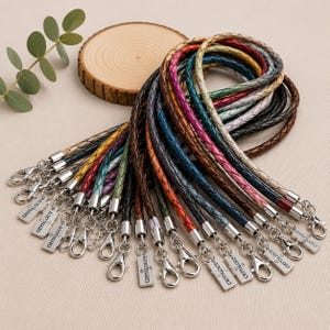 Pode incluir: Uma cole&ccedil;&atilde;o de cord&otilde;es de couro tran&ccedil;ado em v&aacute;rias cores, incluindo marrom, preto, azul, verde, rosa e tons met&aacute;licos. Cada cord&atilde;o possui um fecho lagosta de metal prateado e uma etiqueta retangular gravada com o texto CRYTHOLOGY.