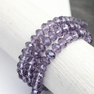 May include: A strand of faceted glass beads in a light purple colour. The beads are round and have a slight oval shape. The beads are strung on a clear thread.