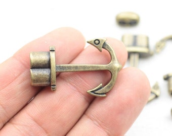 Könnte beinhalten: Ein bronzefarbener Anker-Anhänger mit einem kleinen, runden, dekorativen Detail oben. Der Anker ist an einem kleinen, zylindrischen Anhänger mit einer strukturierten Oberfläche befestigt.
