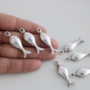 May include: Six silver fish charms with a loop at the top for attaching to jewelry or other crafts.