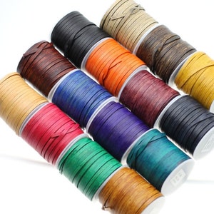 May include: Assortment of leather cord spools in various colors, including black, brown, orange, blue, red, green, and natural. The cords are wound tightly on the spools, creating a colorful and textured display.