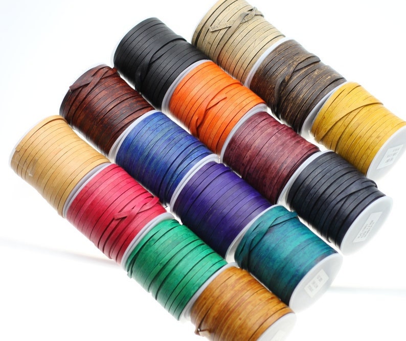 May include: Assortment of leather cord spools in various colors, including black, brown, orange, blue, red, green, and natural. The cords are wound tightly on the spools, creating a colorful and textured display.