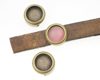 May include: Three antique gold-toned metal settings for cabochons, one with a pink cabochon, on a brown leather strap.
