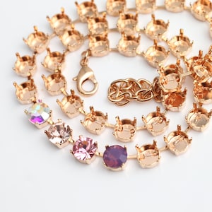 Pode incluir: Uma corrente de ouro com um fecho e engastes para strass. A corrente tem vários strass em tons de rosa e roxo.