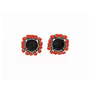 May include: Two square earrings with a central black setting, encircled by small, bright red stones. The earrings have a silver-coloured metal base. The image shows the earrings against a white background.
