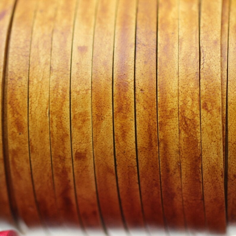 May include: Close-up of a roll of thin, light brown leather strips. The leather has a slightly textured surface and a warm, natural color.