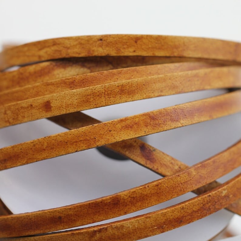 May include: Close-up of a brown leather cord, showing the texture and grain of the leather. The cord is woven in a criss-cross pattern.