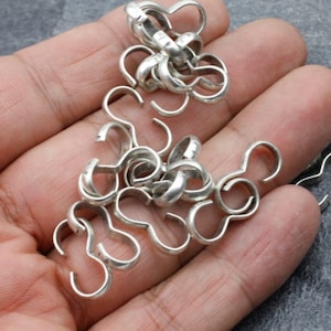 May include: A pile of silver-toned metal jump rings, also known as connecting rings, for jewelry making.