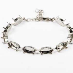 May include: Silver bracelet with oval-shaped settings for gemstones. The bracelet has a lobster claw clasp.