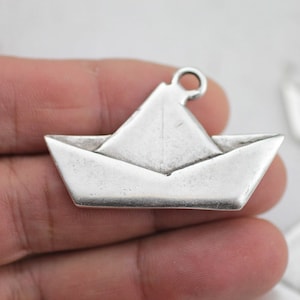 Puede incluir: Encanto de plata en forma de barco de papel doblado. El encanto tiene un bucle en la parte superior para sujetarlo a un collar o pulsera.