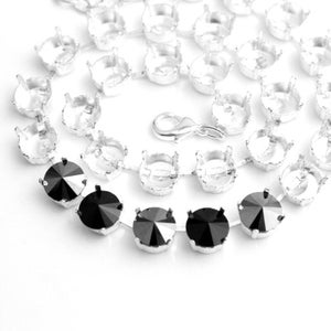 Op de afbeelding: Een zilveren ketting met zwarte kristallen accenten. De ketting is gemaakt van kleine, ronde schakels en heeft een sluiting.
