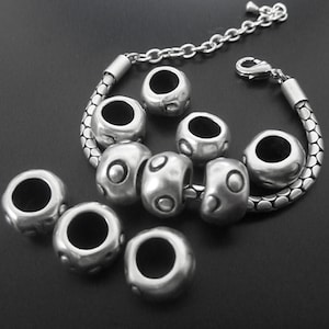 Puede incluir: Pulsera de plata con cadena de plata y múltiples cuentas de plata con superficie texturizada. Las cuentas tienen un agujero circular en el centro.