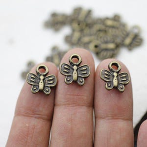 Puede incluir: Tres abalorios de mariposa de color dorado antiguo con un bucle en la parte superior para sujetarlos a joyas u otras manualidades.