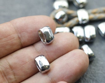 Könnte beinhalten: Nahaufnahme von mehreren glänzenden, silberfarbenen Metallperlen. Die Perlen sind rechteckig mit abgerundeten Kanten und einem Loch in der Mitte. Die Perlen sind wahrscheinlich für die Schmuckherstellung oder andere Bastelarbeiten gedacht.