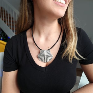 Op de afbeelding: Een zilveren schelp hanger ketting op een zwart leren koord. De hanger is groot en gedetailleerd, met een getextureerd oppervlak.