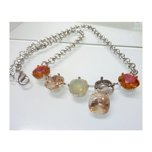 Puede incluir: Un collar plateado con una serie de gemas cuadradas de colores en tonos naranja, melocotón y amarillo pálido. El collar tiene un diseño de eslabones de cadena y un cierre de mosquetón.