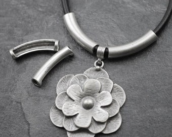 May include: A silver necklace with a flower pendant and two silver end caps. The necklace is made of leather cord and has a silver tube clasp.