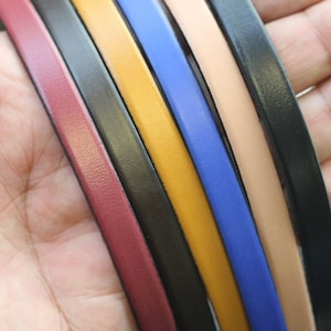 May include: Six leather strips in different colors, including burgundy, black, yellow, blue, and beige, are arranged in a fan shape. The strips are smooth and have a slight sheen.