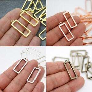 May include: A collection of rectangular metal frame charms in gold, rose gold, silver, and antique bronze finishes. Each charm has a small loop at the top for attaching to jewelry or other crafts. The charms are shown in a variety of hand-held arrangements.