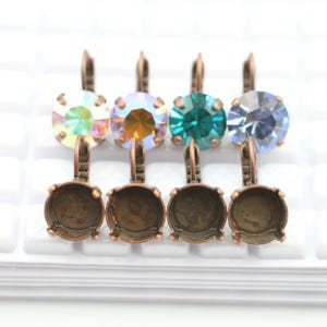 Puede incluir: Cuatro engastes de pendientes de cobre con piedras de cristal de diferentes colores. Los engastes son redondos y tienen un engaste de bisel. Las piedras de cristal son iridiscentes, azul verdoso, azul claro y transparentes.