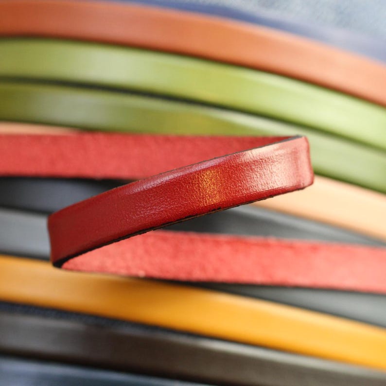 May include: A close-up of a stack of colorful leather strips. The top strip is a bright red and is curved to show the texture of the leather.
