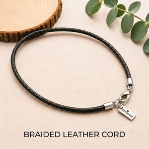 Pode incluir: Um cord&atilde;o de couro tran&ccedil;ado preto com um fecho lagosta de metal prateado e uma etiqueta retangular de metal prateado gravada com o texto CRYSTALOGY. O cord&atilde;o &eacute; finalizado com ponteiras de metal prateado em ambos os lados.