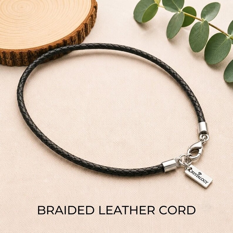 Pode incluir: Um cord&atilde;o de couro tran&ccedil;ado preto com um fecho lagosta de metal prateado e uma etiqueta retangular de metal prateado gravada com o texto CRYSTALOGY. O cord&atilde;o &eacute; finalizado com ponteiras de metal prateado em ambos os lados.