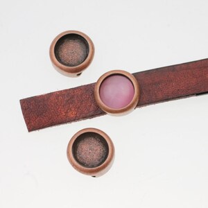 Puede incluir: Tres ajustes de metal de color cobre para un brazalete de cuero. Un ajuste tiene un cabujón de vidrio rosa.