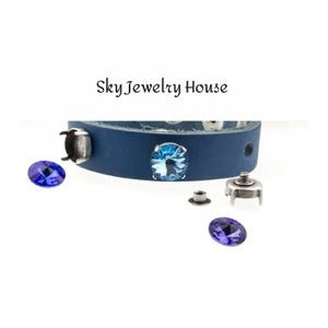 以下が含まれることがあります： ネイビーブルーの革製ブレスレット。シルバーカラーの金具と、青と紫のクリスタル装飾が施されています。「Sky Jewelry House」の文字がブレスレットの上に表示されています。