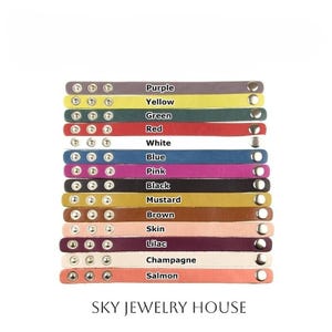 May include: A selection of leather bracelets in a range of colours: purple, yellow, green, red, white, blue, pink, black, mustard, brown, skin, lilac, champagne, and salmon. Each bracelet features silver rivets and a snap closure. The text "SKY JEWELRY HOUSE" is visible.