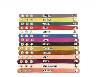 May include: A selection of leather bracelets in a range of colours: purple, yellow, green, red, white, blue, pink, black, mustard, brown, skin, lilac, champagne, and salmon. Each bracelet features silver rivets and a snap closure. The text "SKY JEWELRY HOUSE" is visible.