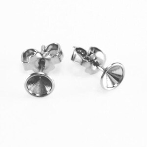 May include: Two silver-colored earring posts with a cup-shaped setting. The posts have a butterfly backing. The settings are designed to hold a gemstone or other decorative element. The earrings are shown on a white background.