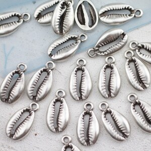 May include: A collection of silver-toned metal charms shaped like cowrie shells. Each charm has a loop at the top for attaching to jewelry or other crafts.