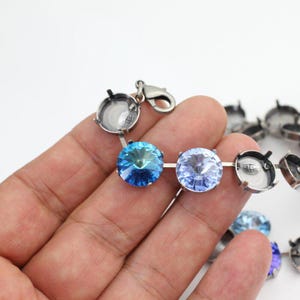 Puede incluir: Un brazalete de cadena plateada con una variedad de piedras de cristal azules y azul claro. El brazalete tiene un cierre de broche.