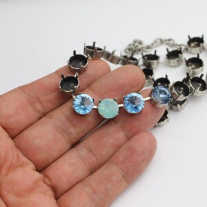 Puede incluir: Un collar plateado con piedras preciosas azul claro y verde pálido. El collar presenta una serie de piedras redondas y facetadas engarzadas en una cadena de metal. Las piedras son una mezcla de azul claro y verde pálido.