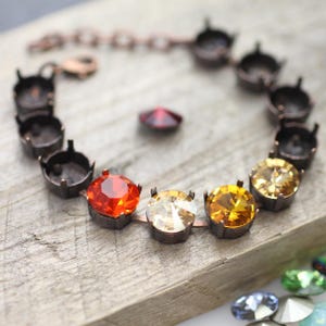 May include: A copper bracelet with a chain link closure and a row of round, faceted gemstones. The gemstones are in shades of orange, yellow, and clear.