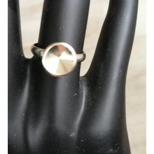 May include: A silver ring with a circular, faceted, gold-colored centerpiece. The ring is displayed on a black surface, showcasing its design and metallic sheen. The ring's band is thin, and the gold-colored centerpiece is the focal point.