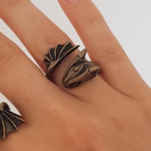 Könnte beinhalten: Ein goldfarbener Drachenring mit detailliertem Kopf und Flügeln. Der Ring ist verstellbar und kann an jedem Finger getragen werden.