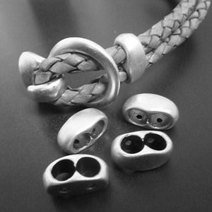May include: Silver metal cord ends with two holes for leather cord. The cord ends are oval shaped and have a smooth, polished finish.