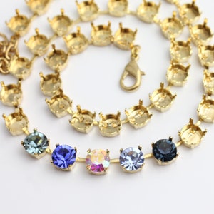 Puede incluir: Un collar de cadena dorada con un cierre y cinco piedras de cristal de diferentes colores. Las piedras de cristal son azules, moradas, iridiscentes y negras.