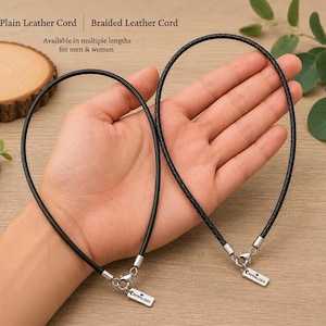 Pode incluir: Dois cord&otilde;es de couro preto, um liso e outro tran&ccedil;ado, cada um com um fecho lagosta de metal prateado e uma pequena etiqueta retangular gravada com o texto Crystalogy. Os cord&otilde;es s&atilde;o projetados como colares com ferragens met&aacute;licas.