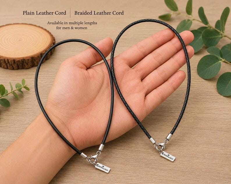 Pode incluir: Dois cord&otilde;es de couro preto, um liso e outro tran&ccedil;ado, cada um com um fecho lagosta de metal prateado e uma pequena etiqueta retangular gravada com o texto Crystalogy. Os cord&otilde;es s&atilde;o projetados como colares com ferragens met&aacute;licas.